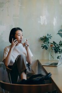 Woman-in-White-Shirt-Sitting-on-Chair-while-Having-Phone-Call-and-drinking-water