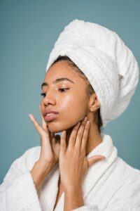 Calm-African-American-female-in-bathrobe-touching-face-against-blue-background